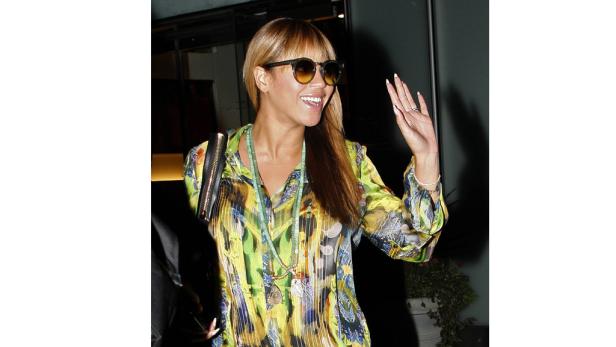 Beyoncé trägt eine gemusterte Bluse, eine Sonnenbrille und winkt.