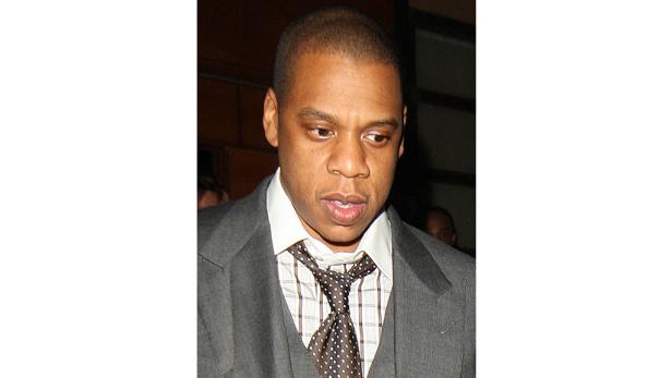 Jay-Z trägt einen grauen Anzug und eine gemusterte Krawatte.