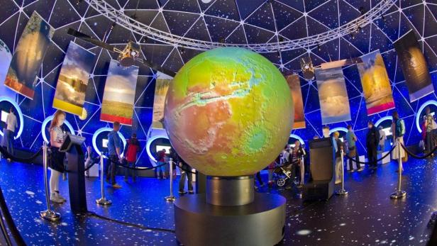 Besucher betrachten eine große, beleuchtete Erdkugel in einer Ausstellung.