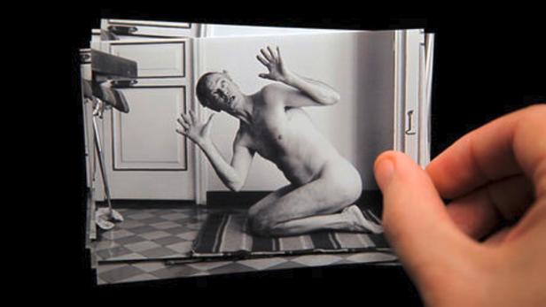 Ein Mann kniet nackt und mit erhobenen Händen auf einer Fotografie.