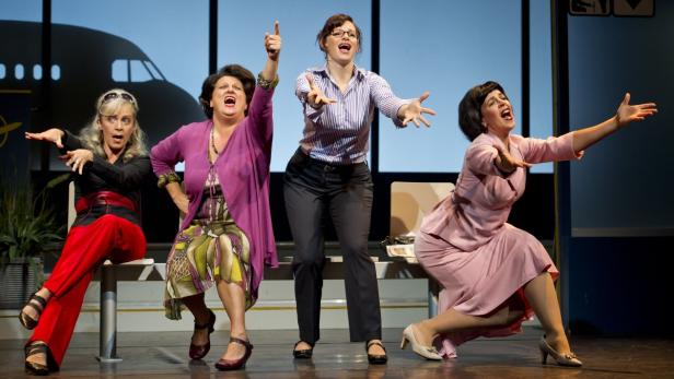 Vier Frauen stehen auf einer Bühne vor einer Flugzeugkulisse und singen.