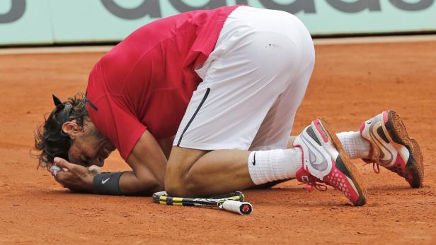 Rafael Nadal kniet enttäuscht auf dem Sandplatz, sein Schläger liegt daneben.