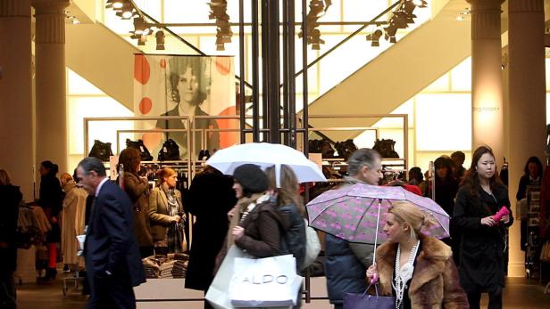 Kunden mit Einkaufstüten und Regenschirmen in einem hellen Kaufhaus.