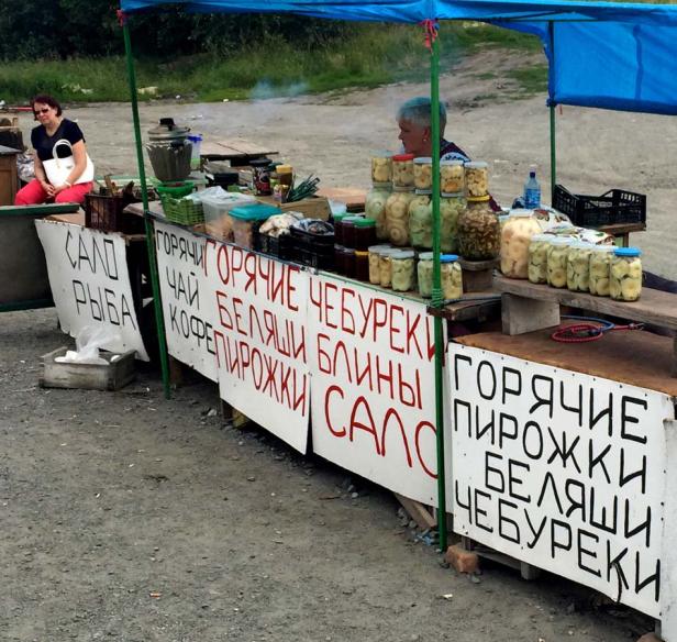 Ein Marktstand unter einem blauen Zelt bietet eingelegtes Gemüse und russische Spezialitäten an.