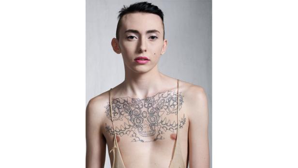 Eine Person mit einem Schädel-Tattoo auf der Brust blickt in die Kamera.