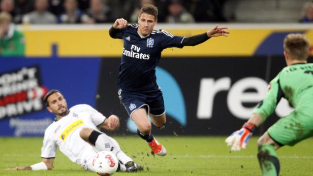 Ein Fußballspieler des Hamburger SV grätscht einen Gegenspieler ab, während der Torwart zusieht.