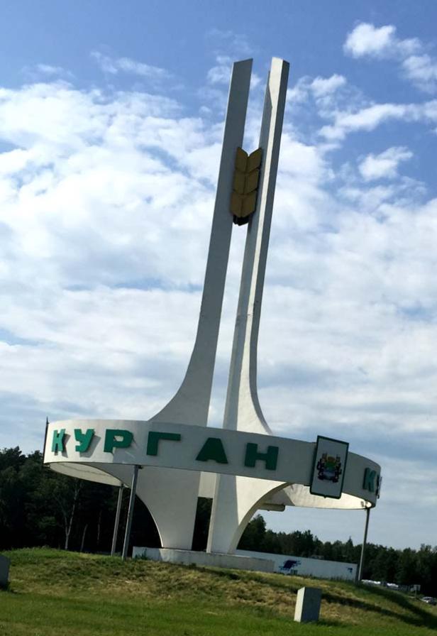 Das Ortseingangsschild von Kurgan, Russland, mit einem stilisierten Weizenähren-Denkmal.