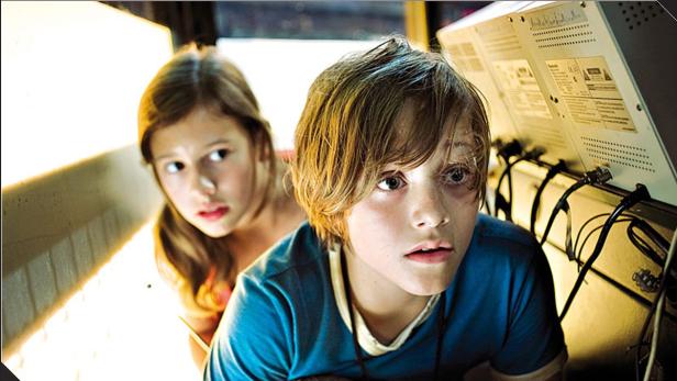 Ein Junge und ein Mädchen schauen mit besorgten Blicken auf einen Apparat mit Kabeln.