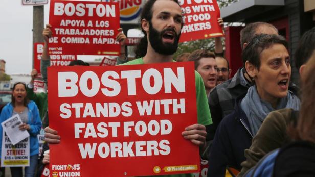 Menschen demonstrieren mit Schildern, auf denen „Boston steht zu Fast-Food-Arbeitern“ steht.