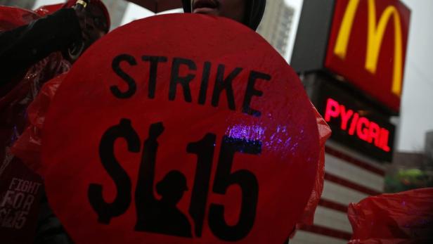 Eine Person hält ein Schild mit der Aufschrift „Strike $15“ vor einem McDonald's-Restaurant.