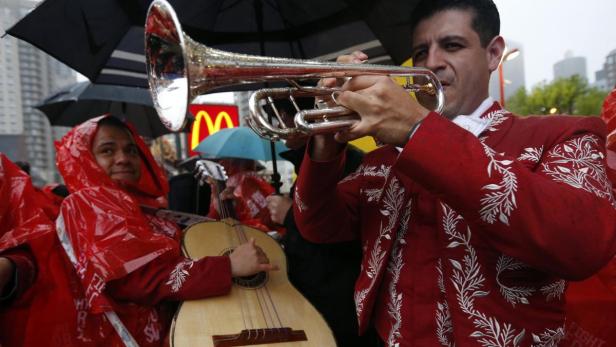 Eine Mariachi-Band spielt im Regen unter Regenschirmen.