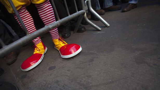 Ein Clown mit rot-weiß gestreiften Strümpfen und übergroßen, rot-gelben Schuhen steht hinter einer Absperrung.