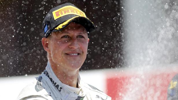 Michael Schumacher lächelt unter einer Dusche aus Champagner.
