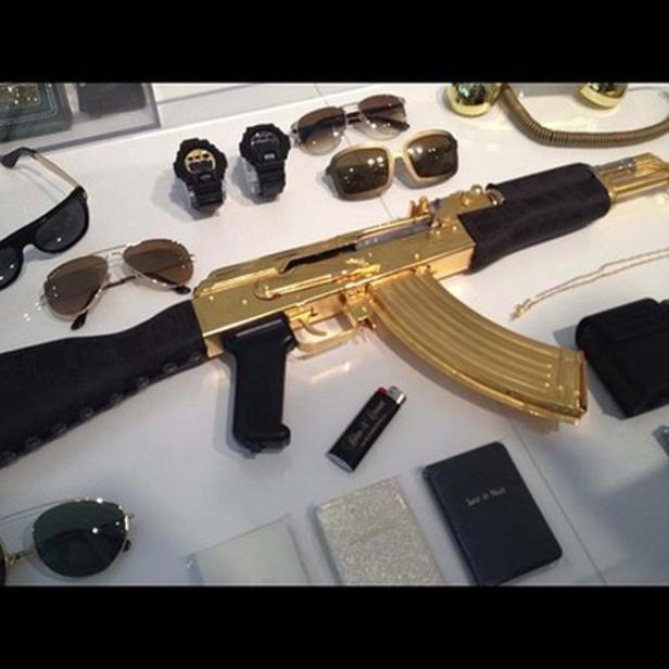 Eine goldene AK-47 liegt zusammen mit Uhren, Sonnenbrillen und anderen Accessoires auf einem Tisch.