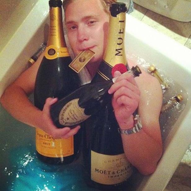 Ein Mann badet in einer Wanne voller Champagnerflaschen.