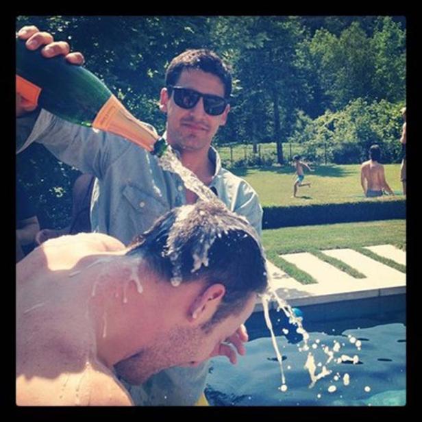 Ein Mann gießt eine Flasche Champagner über den Kopf eines anderen Mannes am Pool.