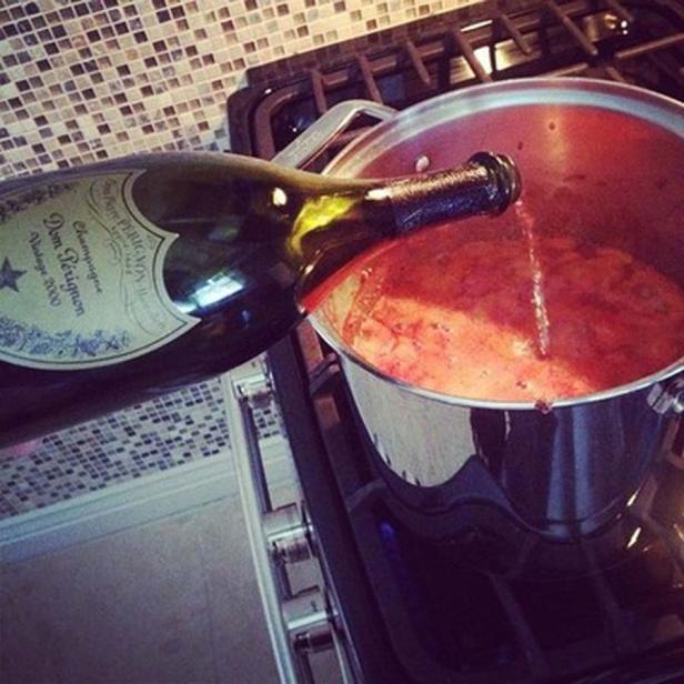 Eine Flasche Dom Pérignon wird in einen Topf mit roter Sauce auf dem Herd gegossen.
