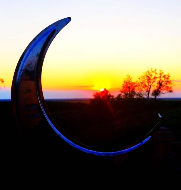 Eine Mondsichel-Skulptur vor einem farbenprächtigen Sonnenuntergang.