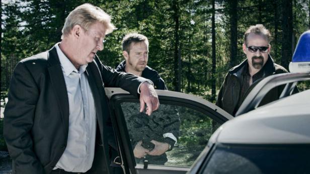 Drei Männer stehen an einem Polizeiauto im Wald.