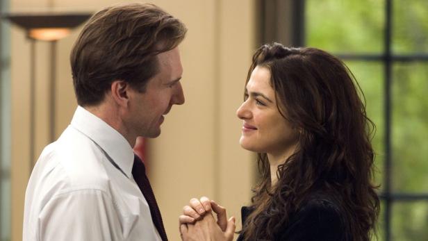 Ralph Fiennes und Rachel Weisz halten Händchen und schauen sich an.