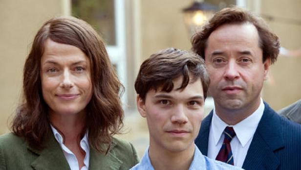 Eine Frau, ein Jugendlicher und ein Mann stehen zusammen vor einem Gebäude.