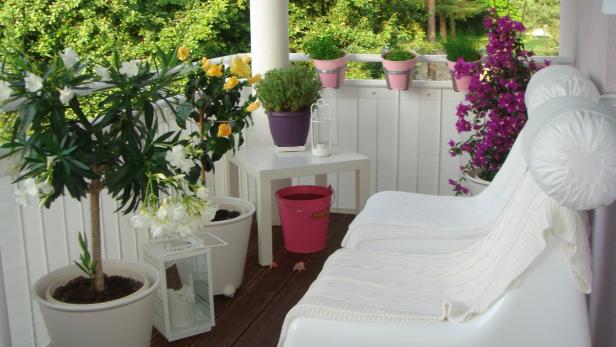 Einladende Terrasse mit weißen Möbeln und blühenden Pflanzen in Töpfen.