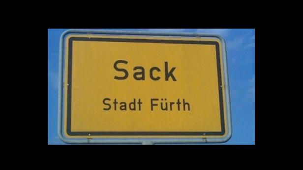 Ein gelbes Ortsschild von Sack, Stadt Fürth, vor blauem Himmel.