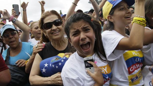 Eine Menschenmenge, viele mit venezolanischen Flaggenfarben, demonstriert und jubelt.