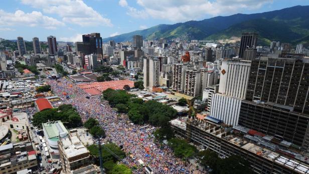 Eine große Menschenmenge versammelt sich in einer Straße in Caracas, Venezuela, vor einer Bergkulisse.