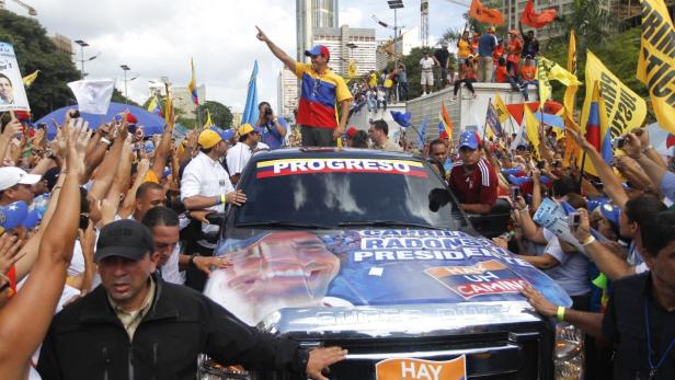 Ein Mann steht auf einem Auto, umgeben von einer Menschenmenge mit venezolanischen Flaggen.