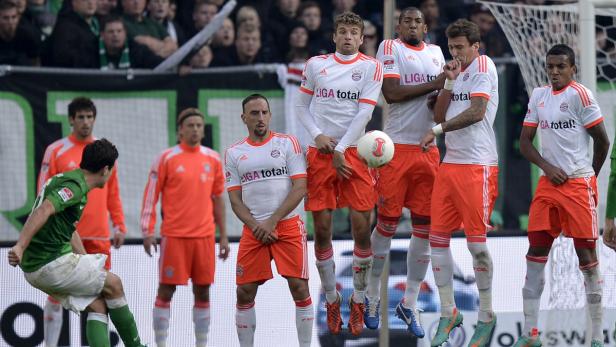 Ein Fußballspieler schießt einen Freistoß, während die gegnerische Mannschaft eine Mauer bildet.