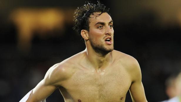 Ein verschwitzter, barfüßiger Mann mit dunklen Haaren blickt zur Seite.