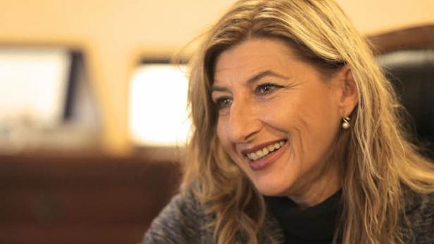 Eine lächelnde Frau mit blonden Haaren und Ohrringen.