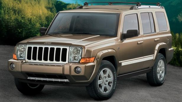 Ein goldfarbener Jeep Commander steht vor einem Wald.