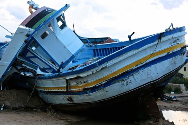 Ein blau-weiß gestreiftes Fischerboot liegt gestrandet an Land.