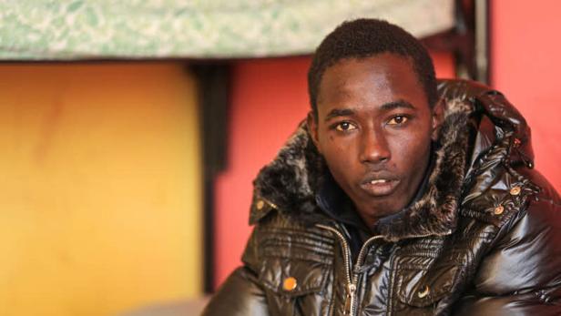 Ein junger Mann mit dunkler Haut trägt eine glänzende, gefütterte Jacke.