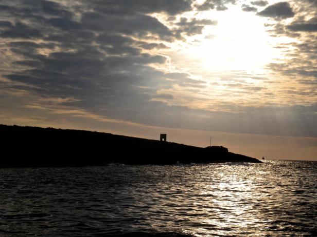 Sonnenstrahlen durchbrechen die Wolken über einer dunklen Küstenlinie.