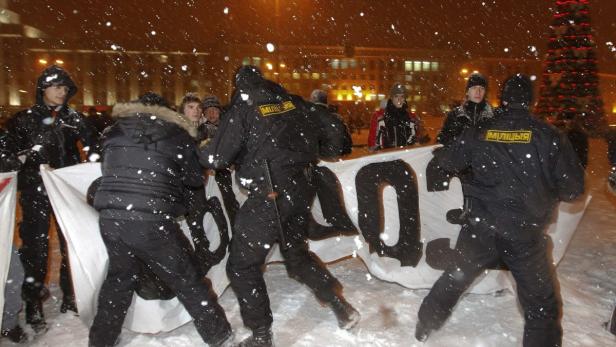 Bei Schneefall halten Polizisten ein Transparent mit kyrillischer Schrift fest.