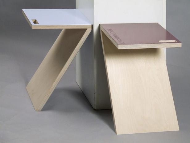 Zwei kleine, moderne Beistelltische aus hellem Holz und farbigen Platten stehen vor einer weißen Wand.