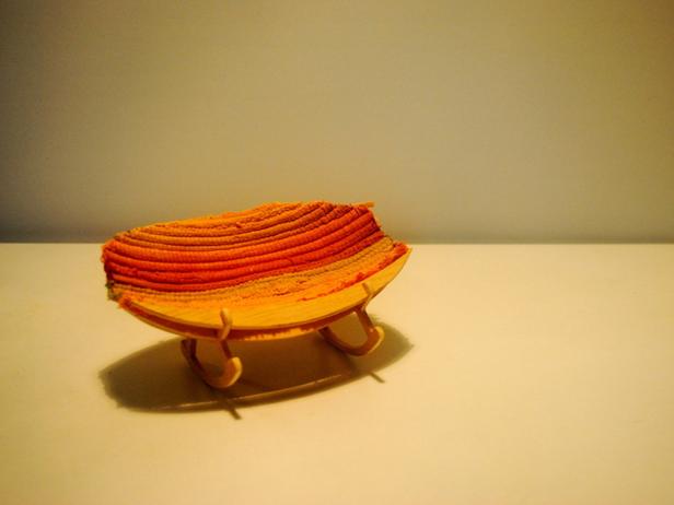 Eine kleine, dekorative Schale aus Holz und orangefarbenem Textil steht auf einem Tisch.