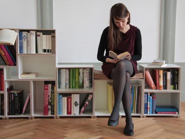 Eine junge Frau sitzt auf einem Bücherregal und liest ein Buch.