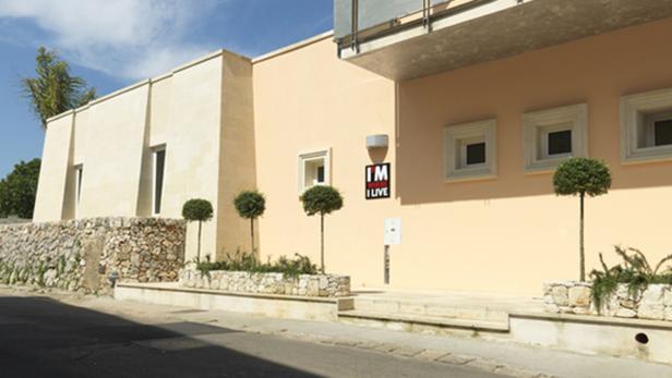 Ein modernes, helles Gebäude mit kleinen, runden Bäumen vor der Fassade.