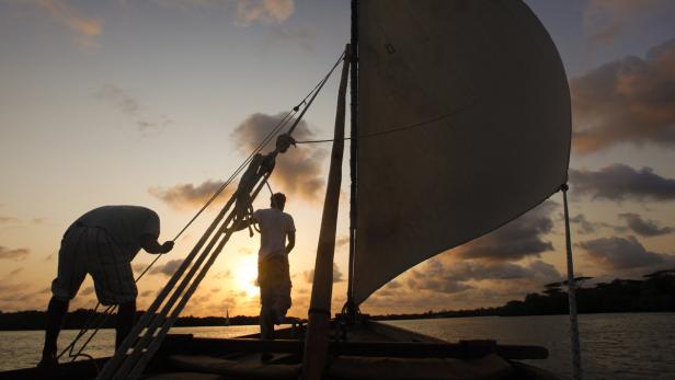 Zwei Männer segeln bei Sonnenuntergang auf einem traditionellen Holzboot.