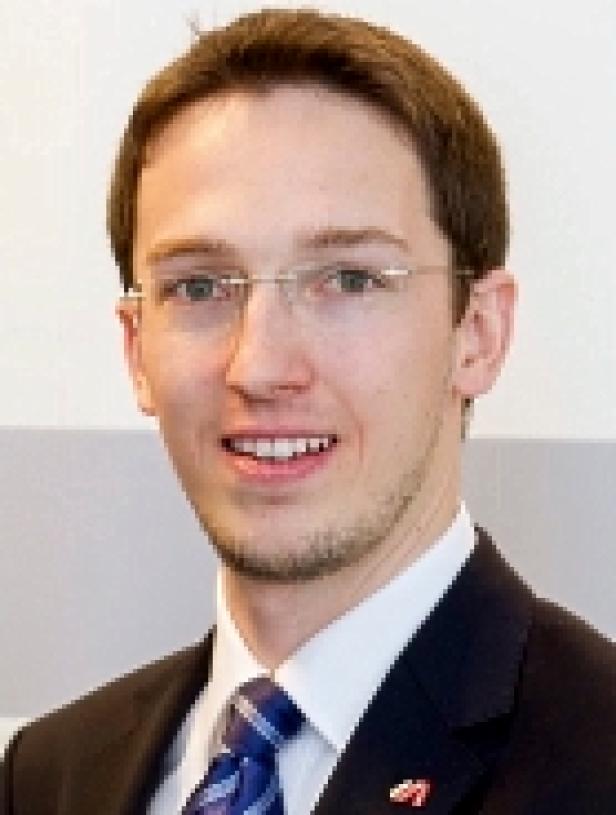 Ein Mann mit Brille und Anzug lächelt in die Kamera.