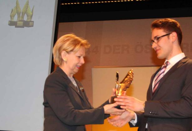 Eine Frau und ein Mann halten gemeinsam eine goldene Trophäe in den Händen.