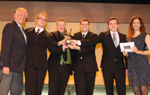 Eine Gruppe von Personen hält eine Trophäe auf einer Bühne.