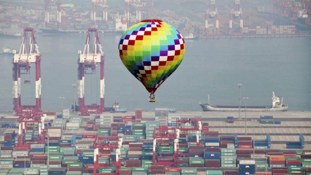 Ein bunter Heißluftballon schwebt über einem Containerhafen.