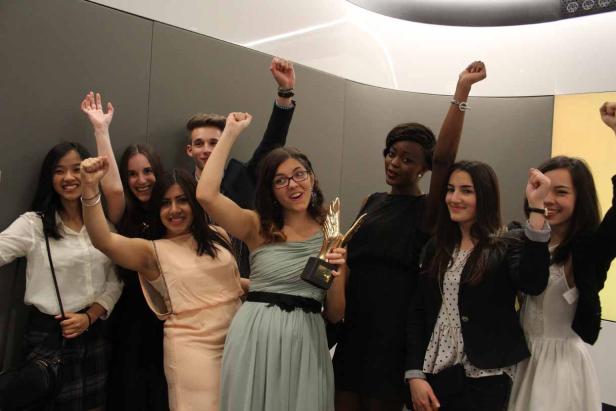 Eine Gruppe junger Leute jubelt mit erhobenen Fäusten und hält eine goldene Trophäe.