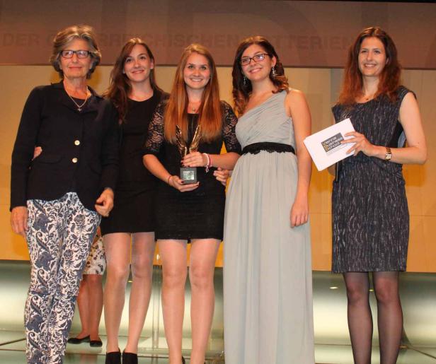 Fünf Frauen posieren auf einer Bühne, eine hält eine Auszeichnung in den Händen.