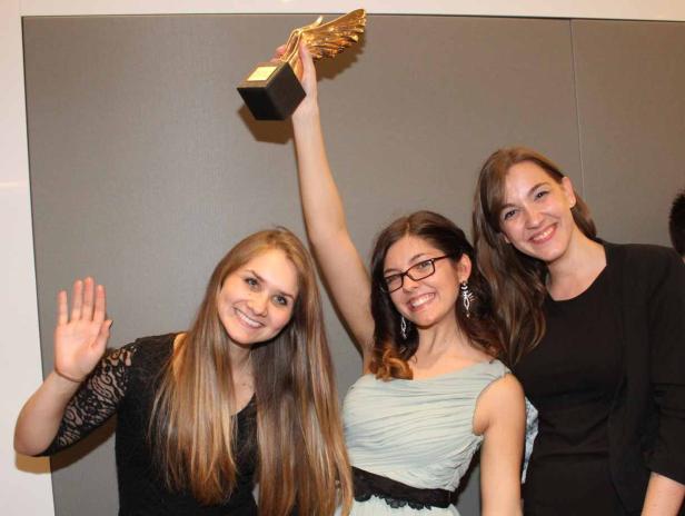 Drei junge Frauen posieren mit einer goldenen Trophäe für ein Foto.